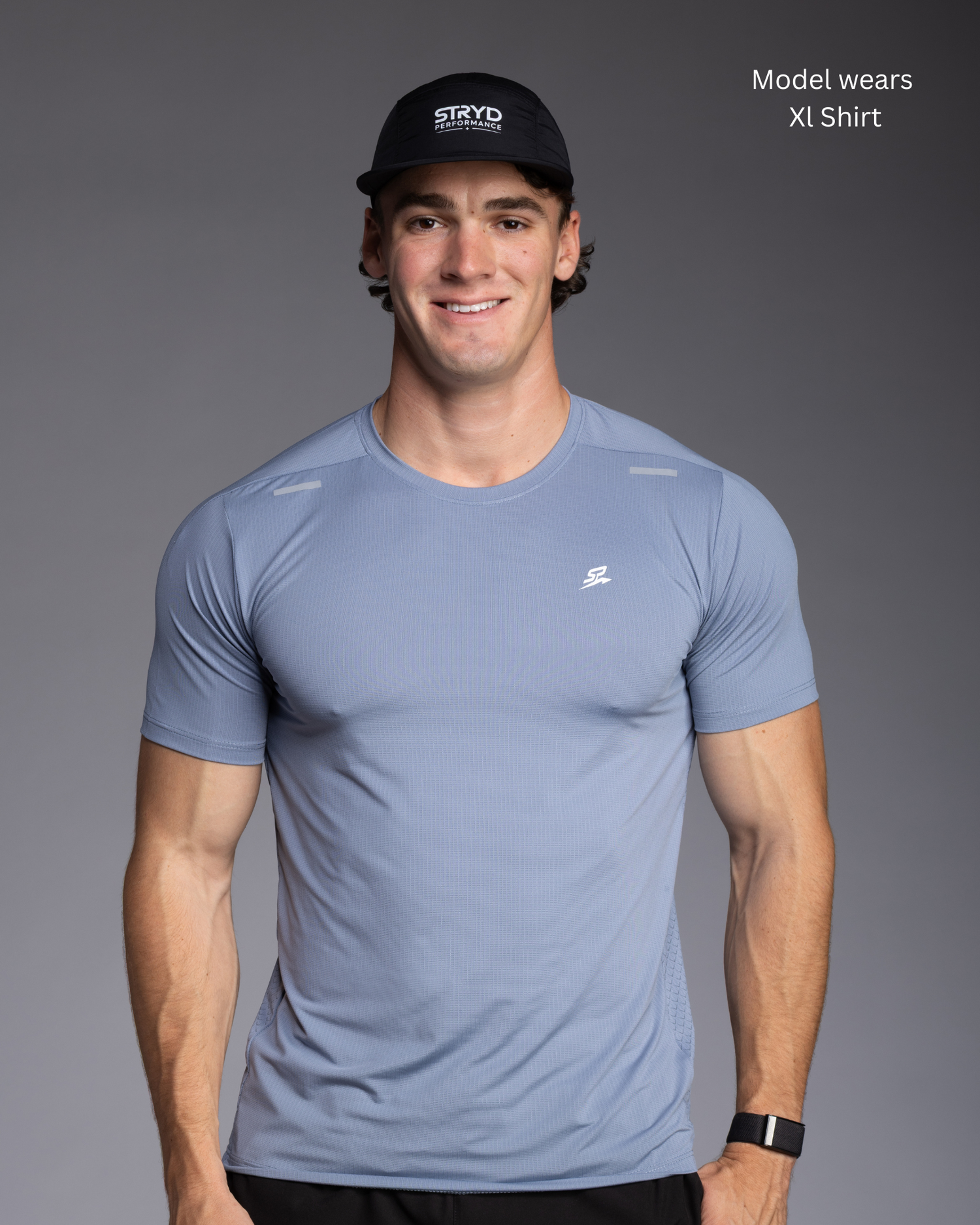 Blue Lightweight sweat wicking running/ active see worn by muscular male model with black running cap standing against grey wall - STRYD Performance