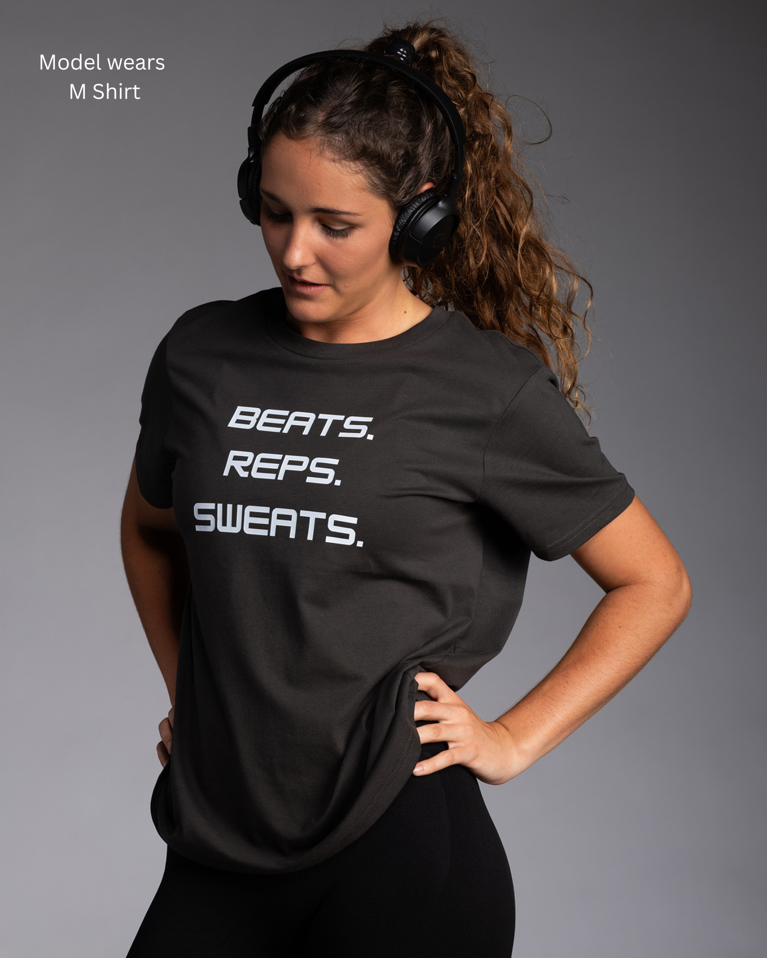 Young fitness model wearing STRYD Performance Icon Graphic print tee in Coal colour that says Beats.Reps.Sweats. Words front