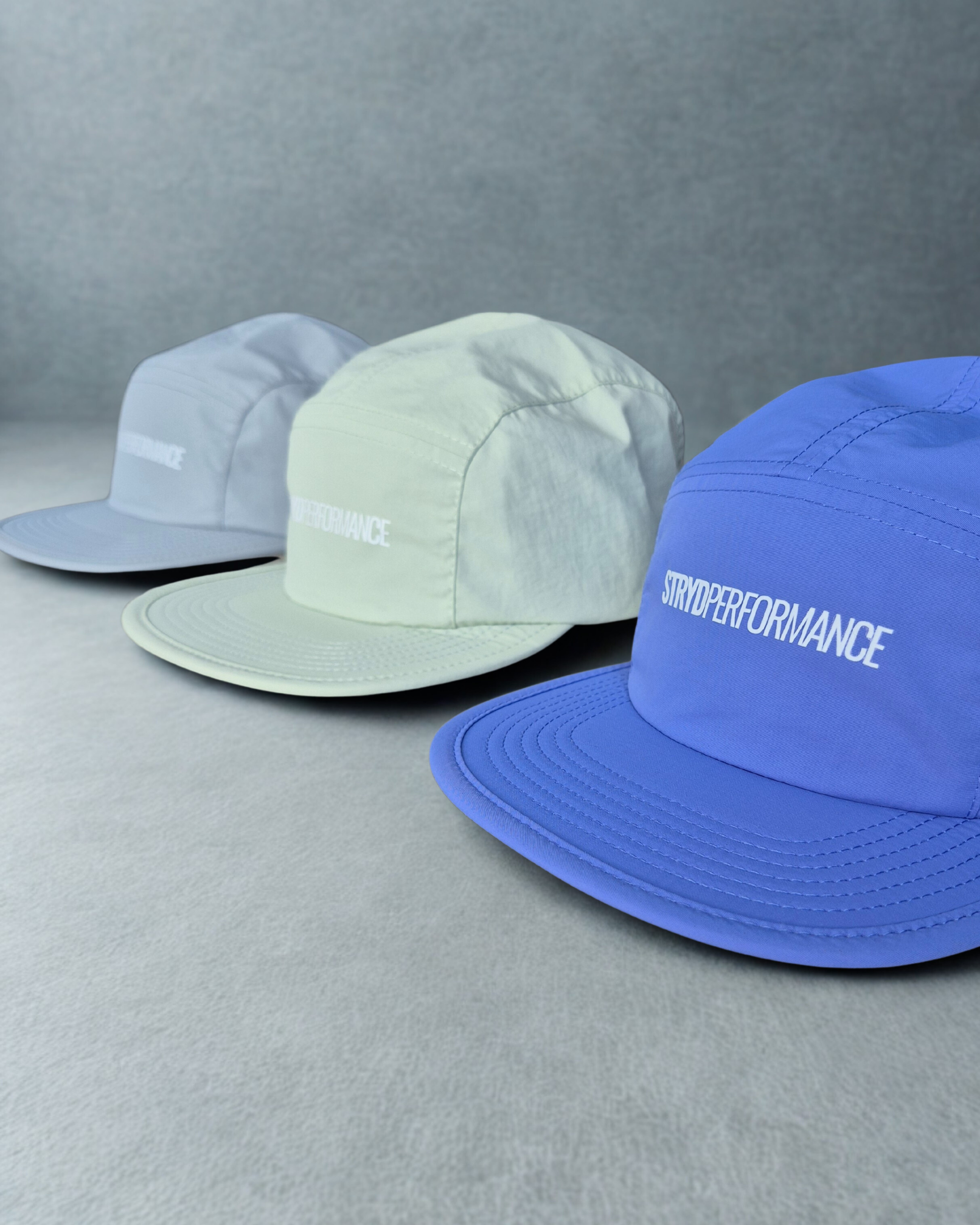 Three hats in blue, green, and gray on a gray background with 'STRYPERFORMANCE' branding.